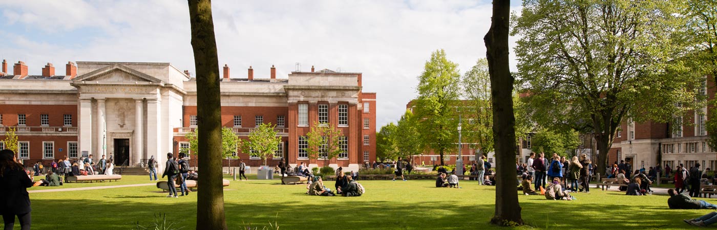 Students sat outside the Samuel Alexander Building on a sunny day