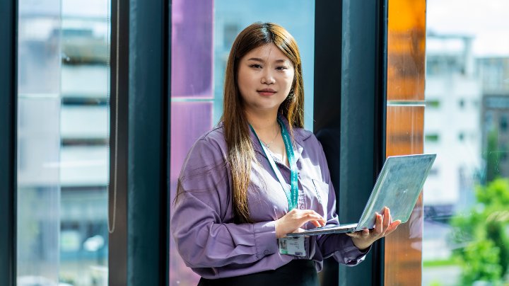 Student holding an open laptop staring at the camera