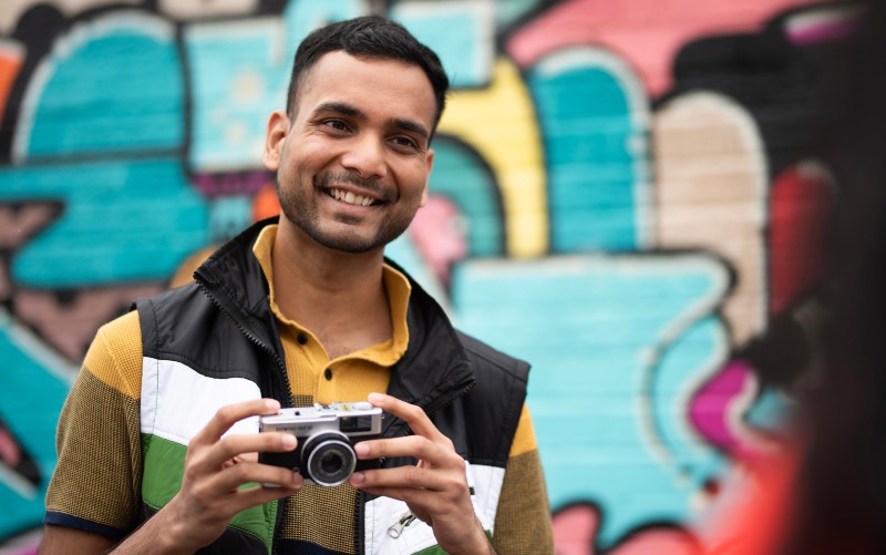 Students smiling to another student whilst holding a camera