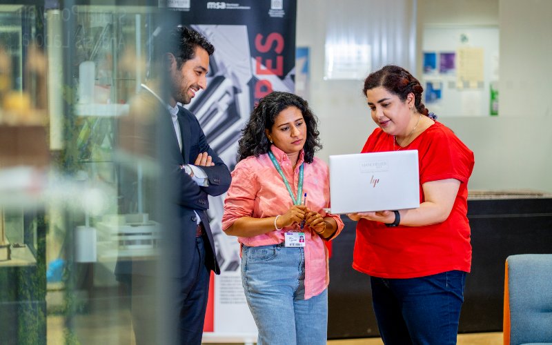 Postgraduate students standing around a laptop