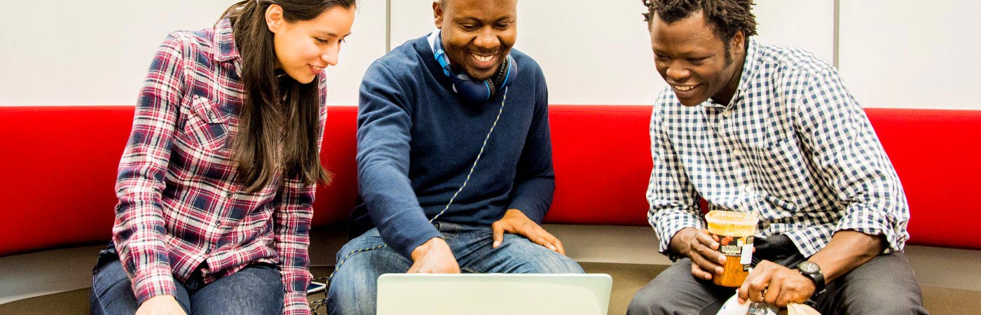 Three students sat around laptop smiling.