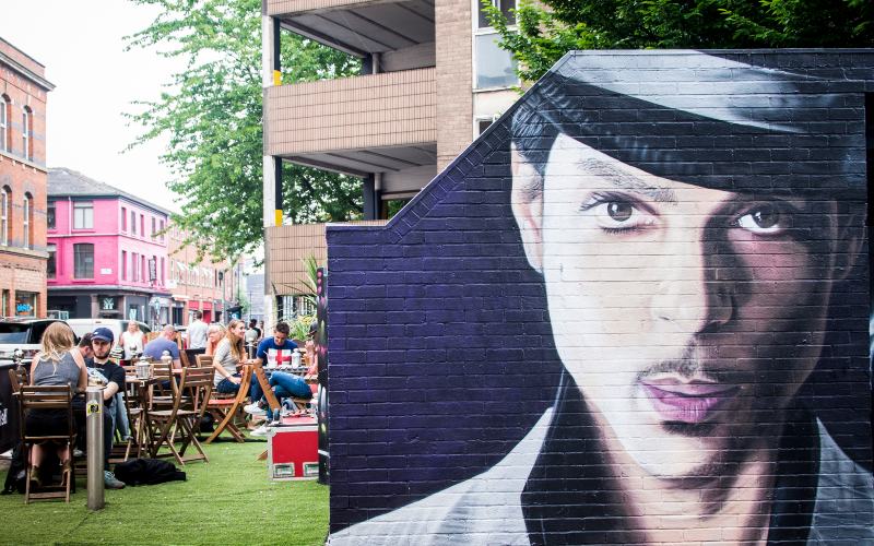 Mural painted on a wall beside a group of people drinking outside