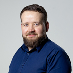 Thomas Flavel - Lecturer in Digital Media and Culture. He wears a blue shirt and smiles at the camera 