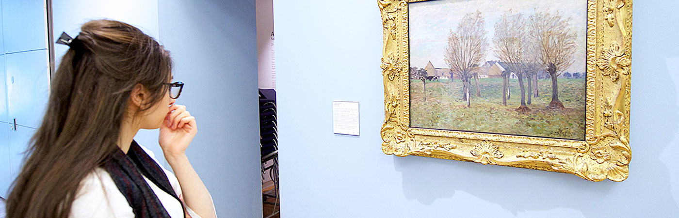 Female student looking a painting on the wall of a gallery