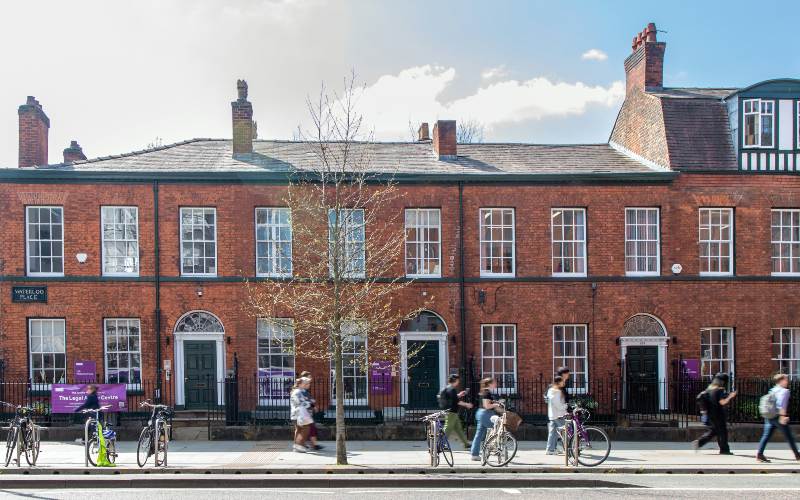 Row of red-brick buildings with tall windows and arched doorways, bicycles along the railings.