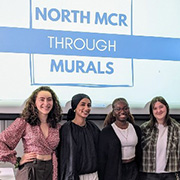 Six young adults smiling in a classroom, standing in front of a screen reading North MCR Through Murals.