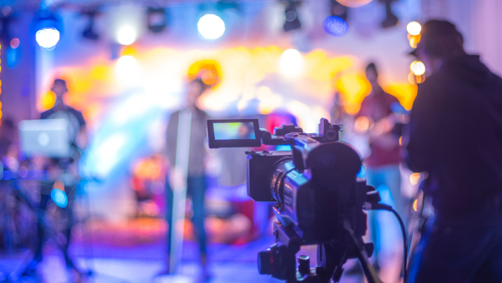 A video camera videoing singers on a stage
