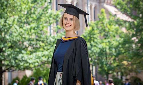 A photo of Laura Nuttall in graduation cap and gown smiling outdoors on the university campus.