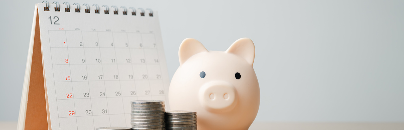 Piggy bank with coins beside a calendar, representing savings and financial planning.