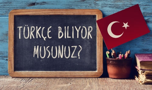 Chalkboard reading Türkçe Biliyor Musunuz? (Do you speak Turkish?) beside a Turkish flag.