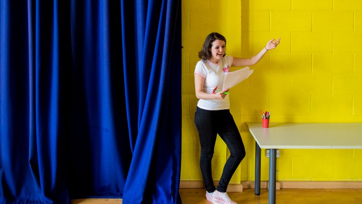 Student practicing acting next to theatre curtains