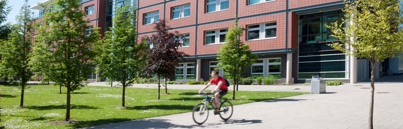 Student riding their bike through the trees and buildings on campus