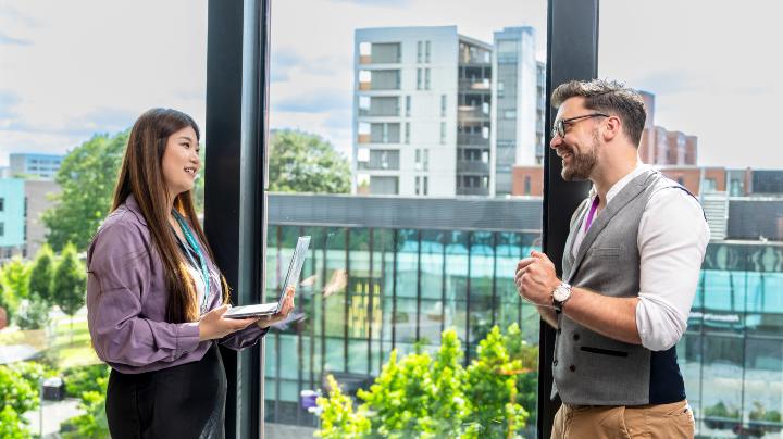 Two members of staff talking in a glass stairwell