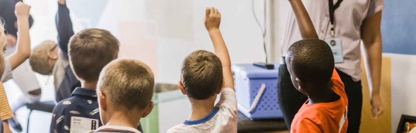 Young students are raising their hands in a classroom. 