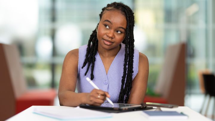 Student holding a pen sat at a desk with books and paperwork on