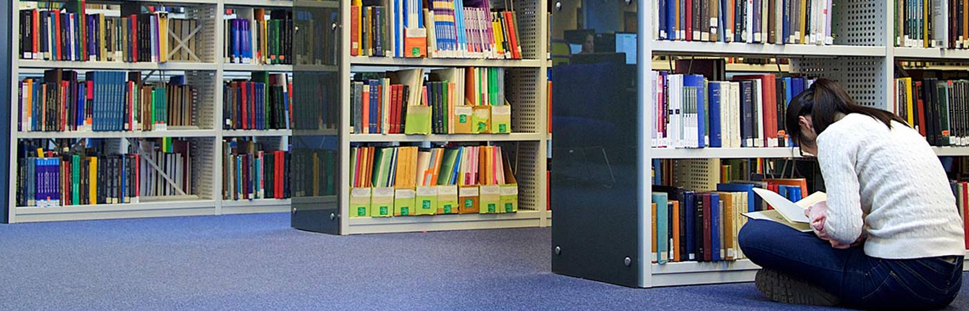 Female student sitting on floor reading a book in the library