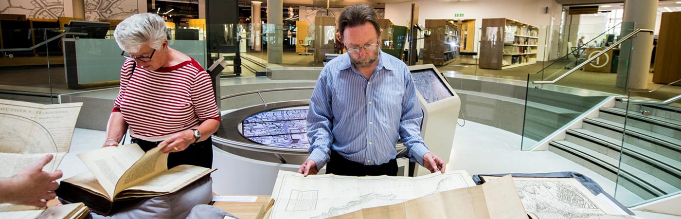 Members of research staff reading old maps in the library