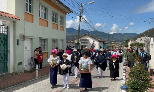 An large group of members of an indigenous community walking down the street in traditional dress