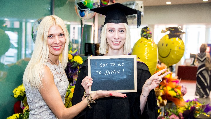 A languages student with a sign that reads 'I got to go to Japan'