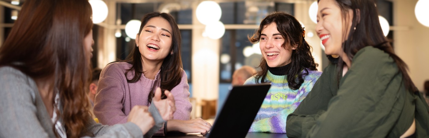 Students sat laughing around a table with a laptop