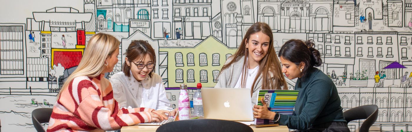 Students sat laughing at a table with a laptop