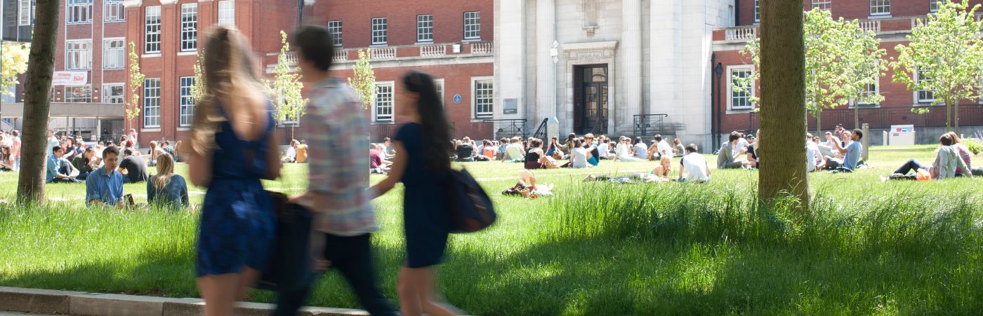 Blurred students walking across campus with groups of students sat on the grass
