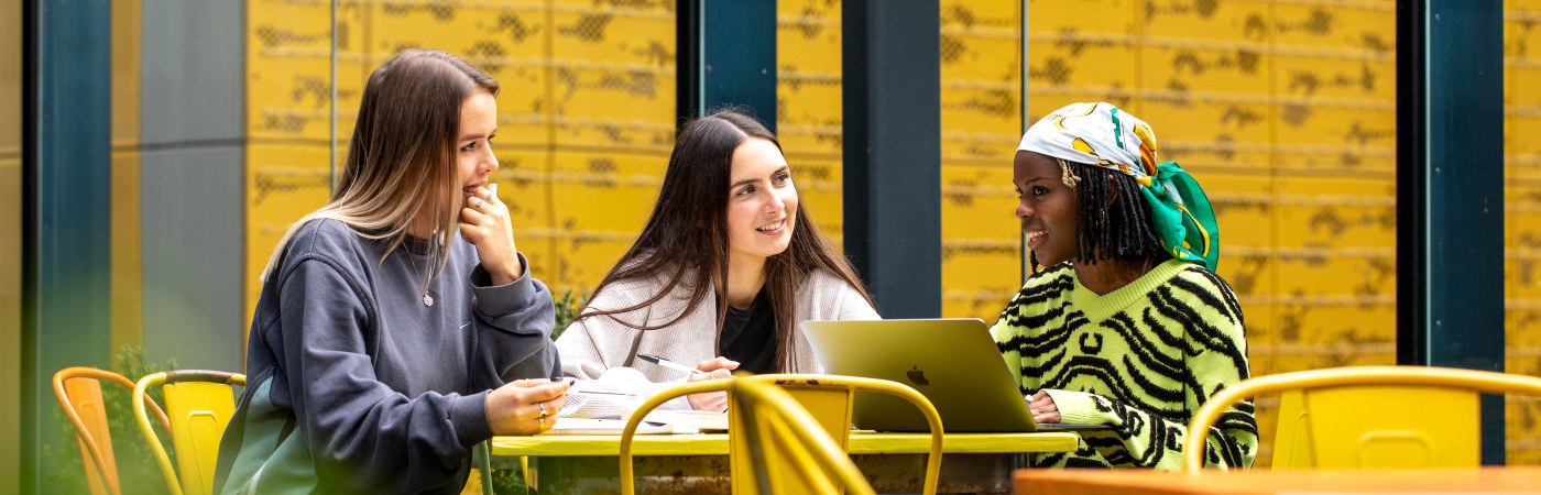 Students sat chatting at a table with a laptop