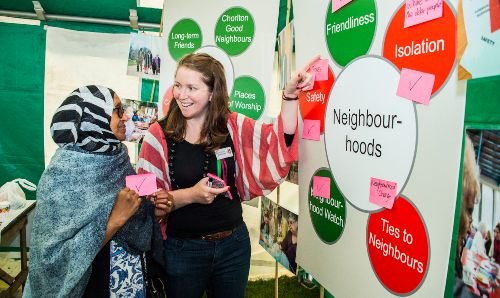 A member of staff talking to a lady in front of a board on neighbourhoods.