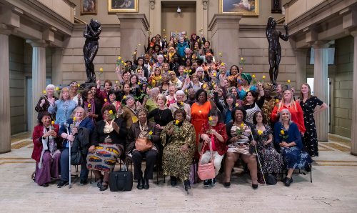 Group of women from Uncertain Futures project holding yellow roses in Manchester Art Gallery.