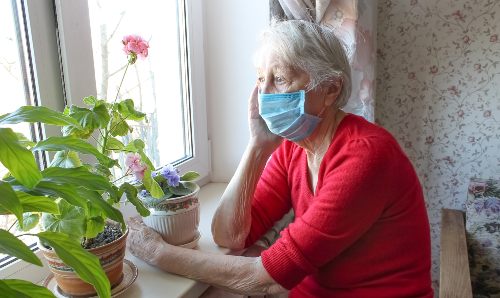 Woman in face mask sat looking out of a house window