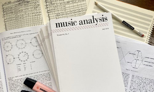 Stack of academic papers and open music theory books on a desk