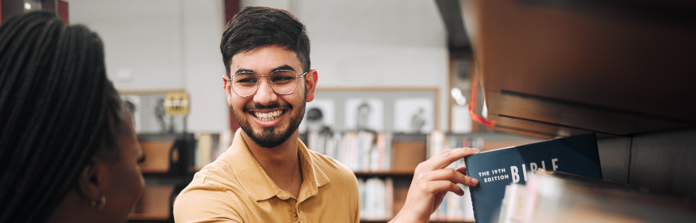 Smiling PGR student picking out a book in a library