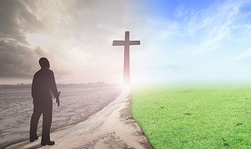 Person stood looking at a bright crucifix in a field, sunny on one side and stormy on the other