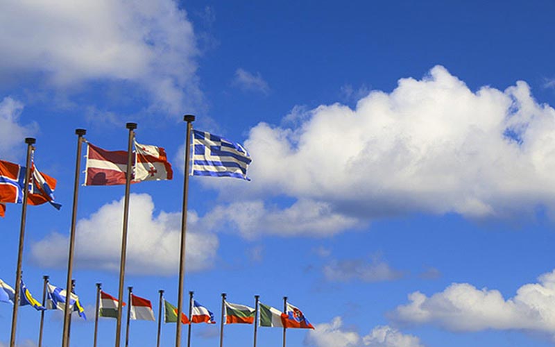 Many country flags on flagpoles blowing in the breeze.