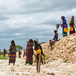 Women in colourful dress collecting water in a barren landscape.