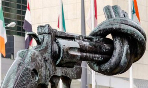 A statue of a gun with the barrel tied in a knot alongside flags