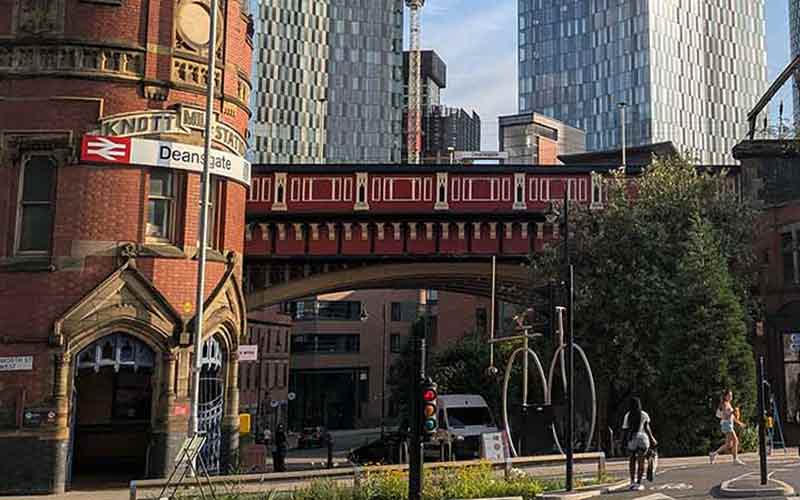 Historic red-brick buildings and railway bridge contrast with modern glass skyscrapers in Manchester