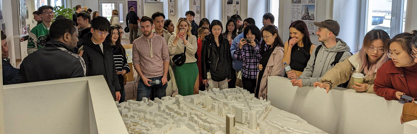 Students observing a detailed white architectural model of a city in a bright exhibition-style room.