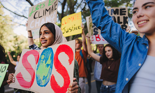 Young climate activists at a rally holding SOS and Climate Justice protest signs outdoors.