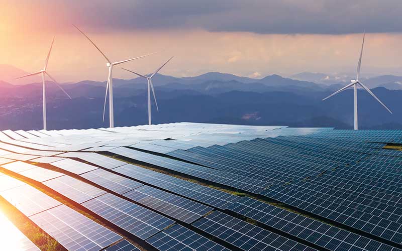 Solar panels and wind turbines at sunset in a mountain landscape generating renewable energy.