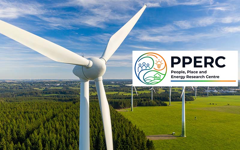 Wind turbines across green fields and forest beneath a blue sky, generating renewable energy.