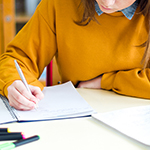 Student sat at a desk, writing in a notebook  