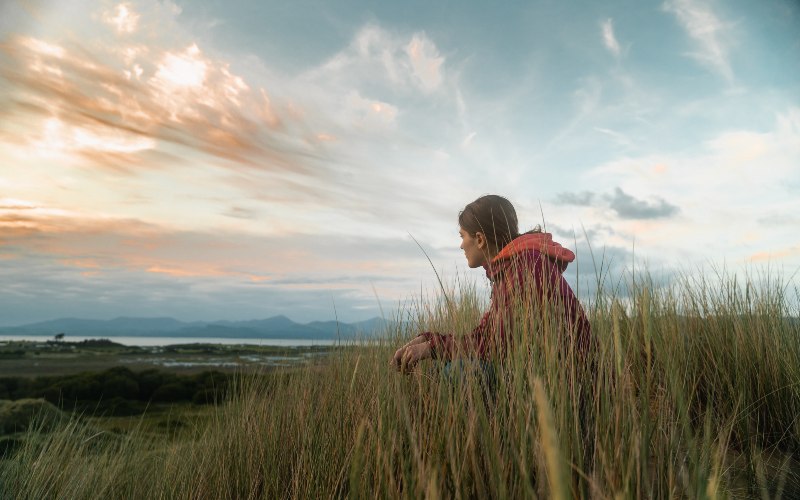 Person sat in reeds at the beach, looking out to sea
