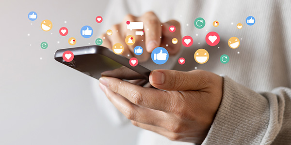 Hands using smartphone with floating social media icons like hearts, likes, and emojis.