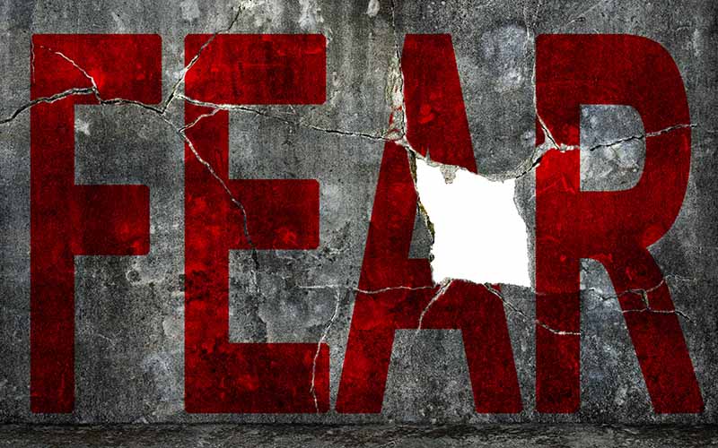 Red word FEAR on a cracked concrete wall, with part of the letter A broken and chipped away.
