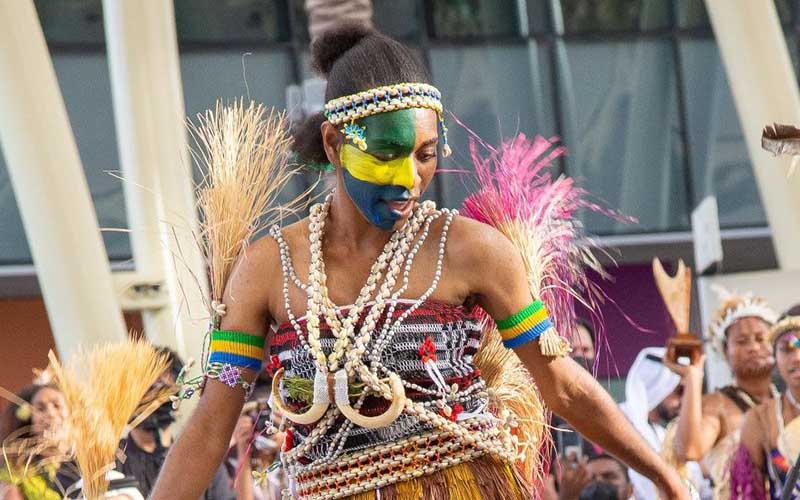 Papua New Guinean woman dances in traditional attire with face paint during cultural performance.