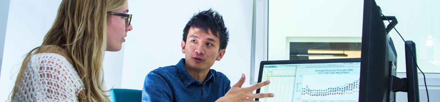 Two people sat in front of dual display monitors looking at economics data