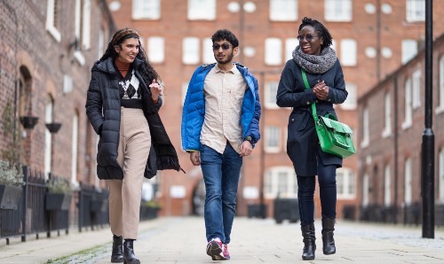Three students laughing and walking down a street in Manchester