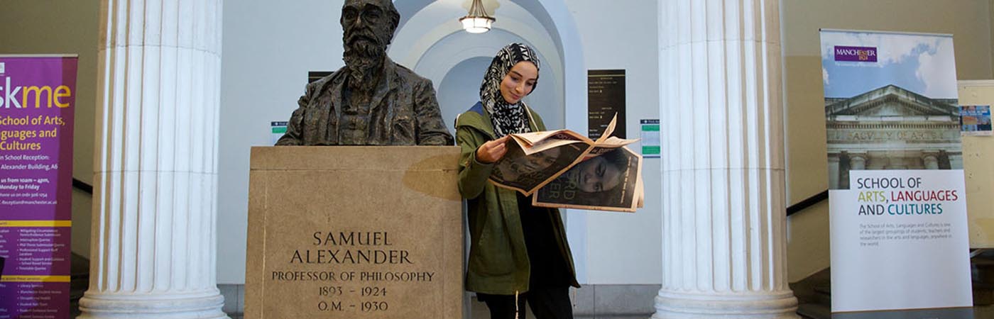 A woman in a headscarf reading a newspaper in beside a statue