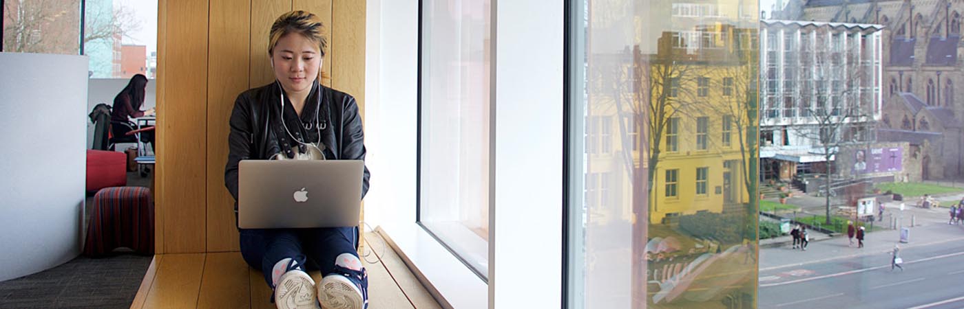 Female sat on laptop near window with headphones in